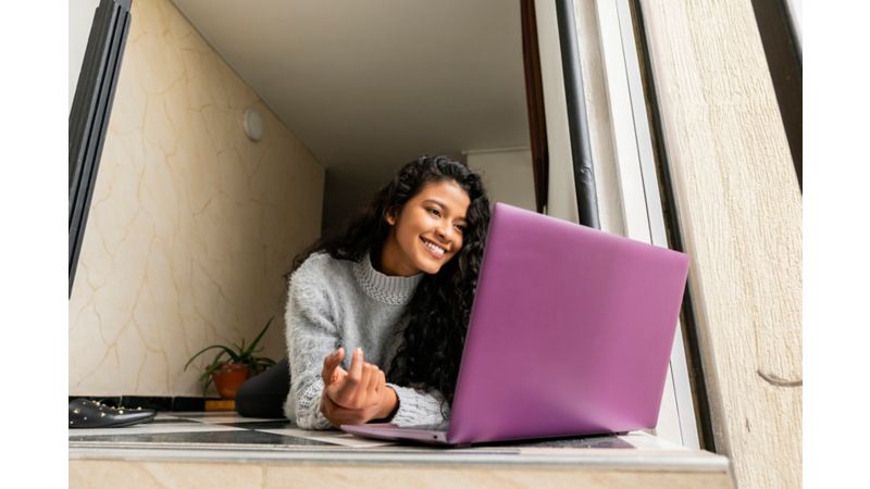 girl laying on hallway floor in grey sweater smiling at purple laptop